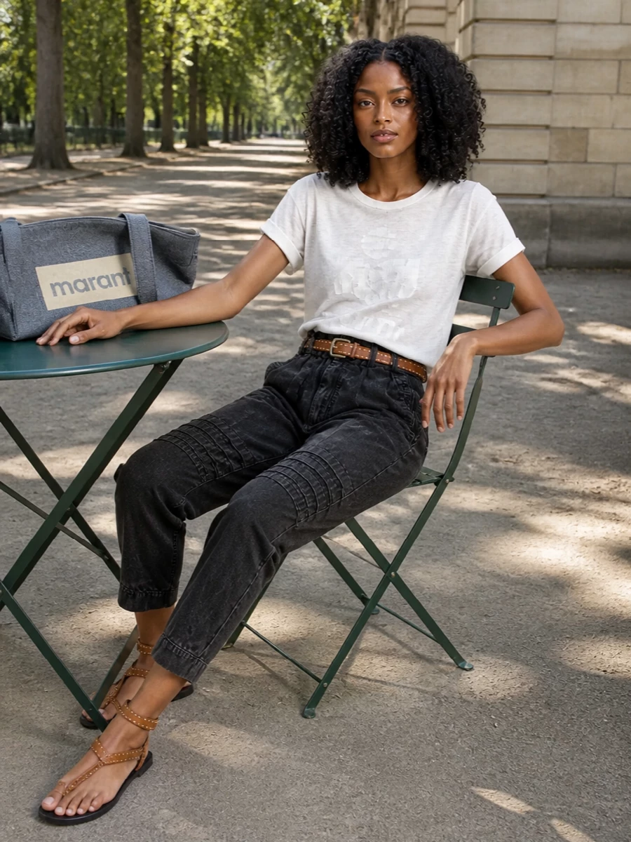 A featherweight marl tee tops washed‑black paperbag trousers for a slouchy, off‑duty silhouette with a sculpted waist. Studded tan sandals and a matching belt bring sun‑worn warmth and attitude, while the slate logo tote adds an easy, slightly sporty finish in cool grey tones.