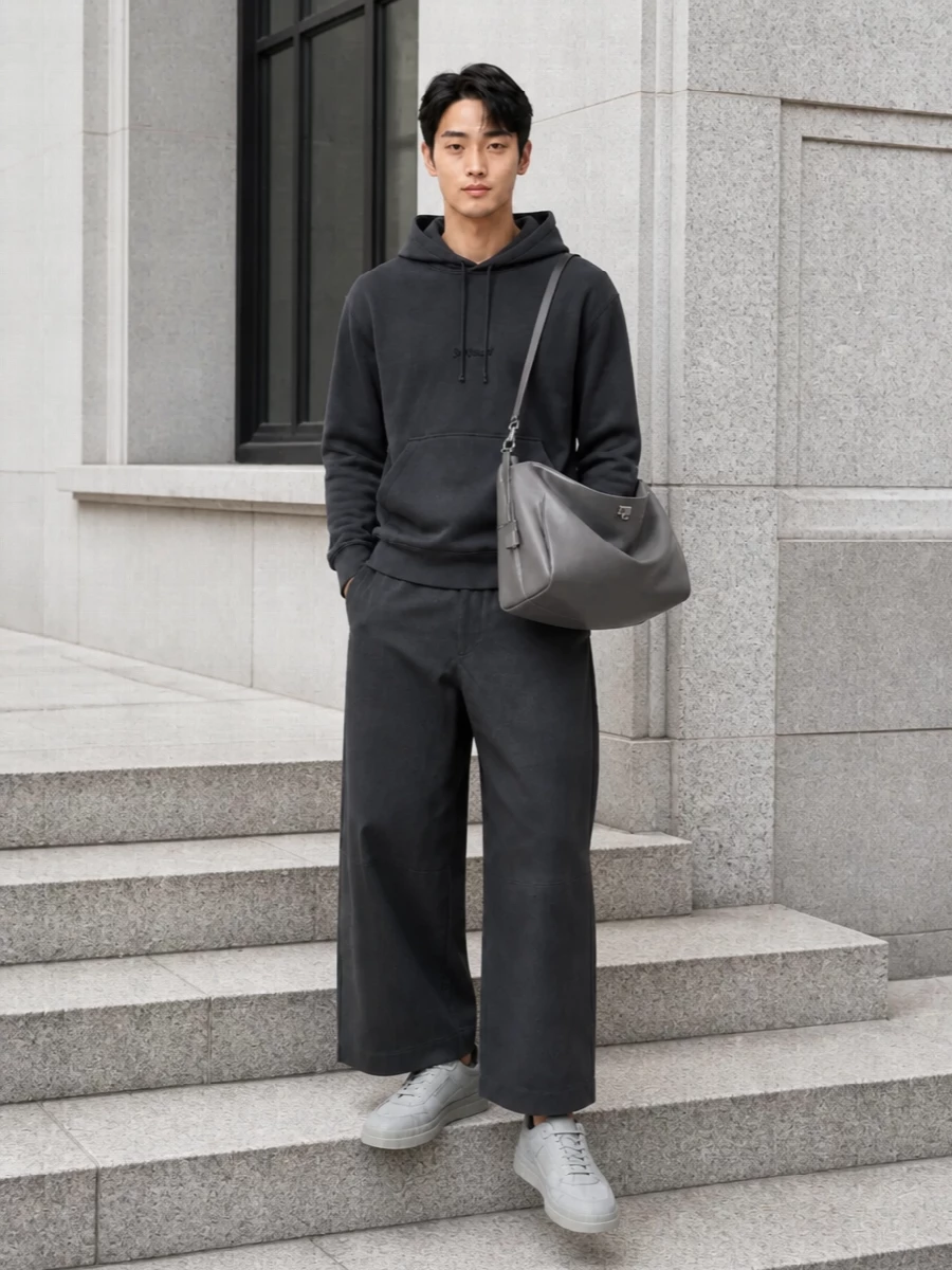 A grayscale street-ready uniform built around clean volume and quiet detailing. The charcoal hoodie and wide cropped trouser create a relaxed, architectural line that lets the grey Balenciaga bag take focus. Tonal ice-grey sneakers keep everything sharp but understated, carrying the monochrome story from head to toe.