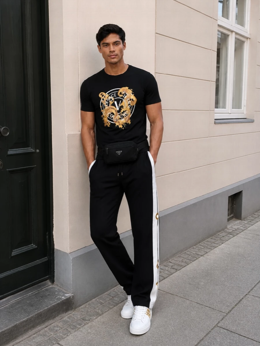 Gold-detailed Versace sneakers ground a black and gold story that feels sharp without trying too hard. The logo tee and striped track pants sit in the sweet spot between athletic and polished, ideal for city days that roll into late-night plans. Black accessories keep everything graphic and pulled together so the hardware and baroque touches do the talking.