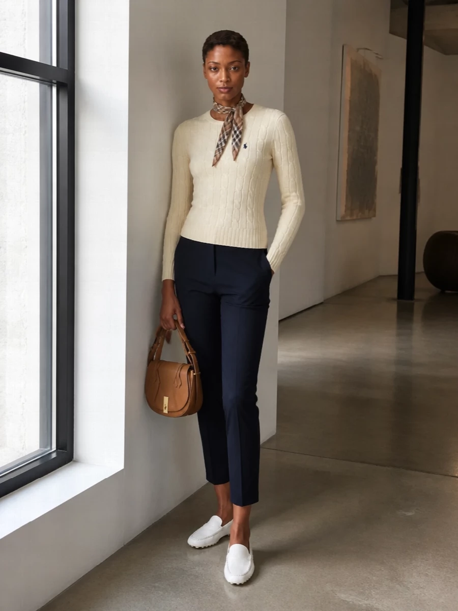 A buttercream cable knit meets slim navy chinos for a clean, collegiate take on smart casual. White driving loafers keep the palette fresh and light, while a tan saddle bag and slender check scarf introduce just enough equestrian richness. The result is quietly polished and relaxed, ideal for city days or coastal weekends where you still want a considered finish.