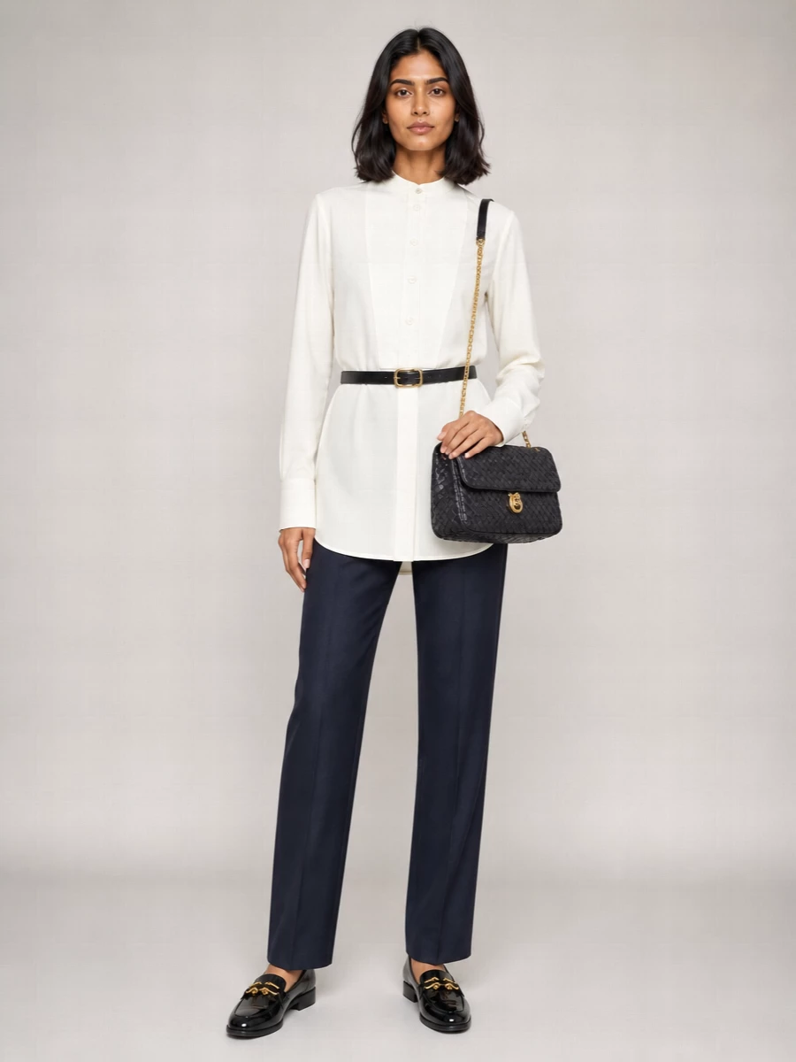 Ink pinstripe trousers are grounded with a longline ivory tuxedo shirt for a clean, precise take on modern tailoring. Navy loafers and a structured black intrecciato shoulder bag keep the palette dark and quiet, while subtle gold hardware adds just enough warmth for client days that turn into dinner. A slim black belt sharpens the waist so the relaxed straight leg reads intentional rather than casual.