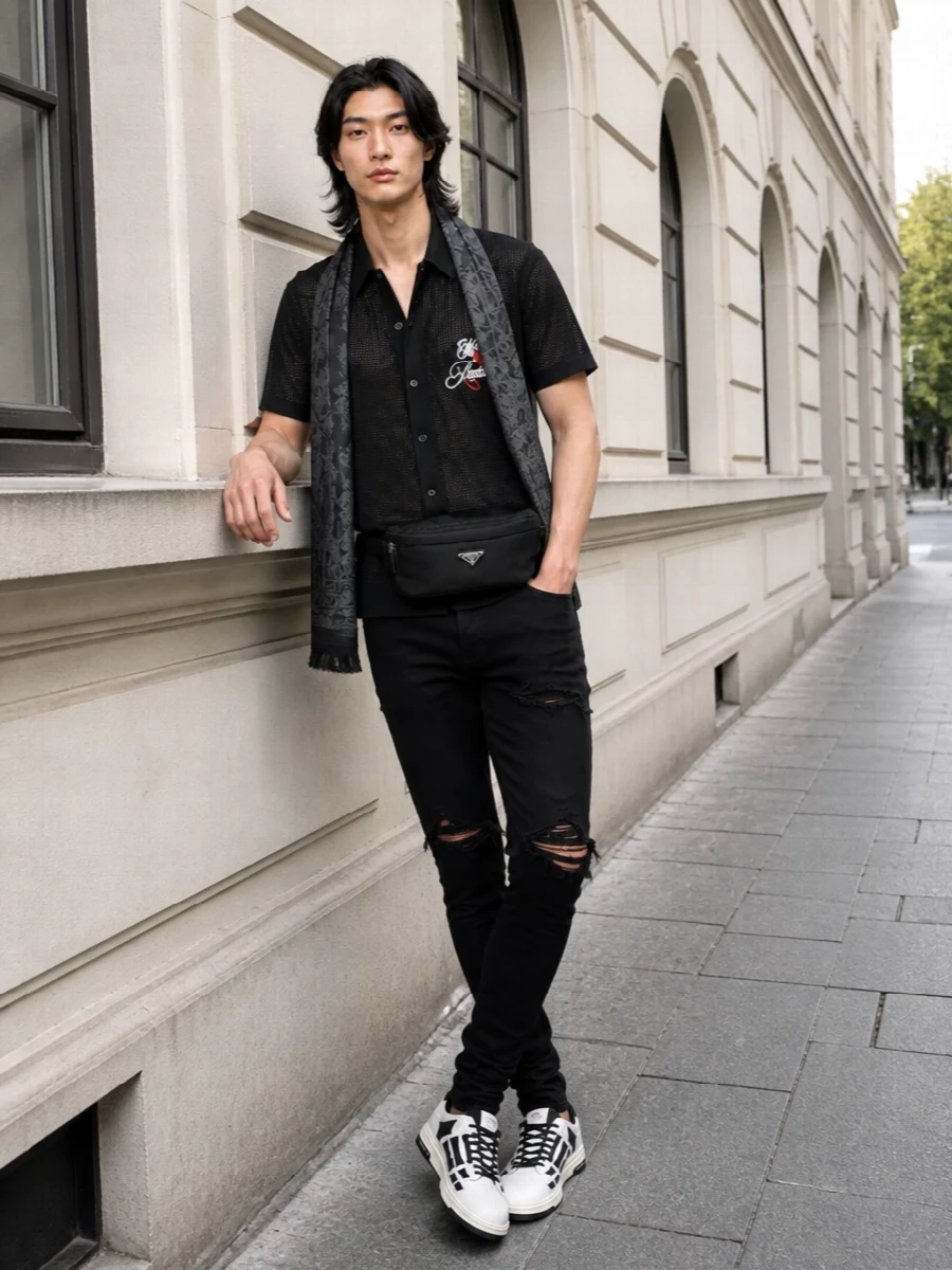 This is a tight, nocturnal Amiri uniform built around the sheer mesh shirt, with jet-black shredded denim sharpening the line and keeping the focus on the torso. Graphic black and white sneakers echo the embroidery so the whole palette reads deliberate, while the Prada belt bag and skull scarf add just enough hardware and texture for a polished, late-city-bar finish. It feels club-ready, high-energy and still composed from head to toe.