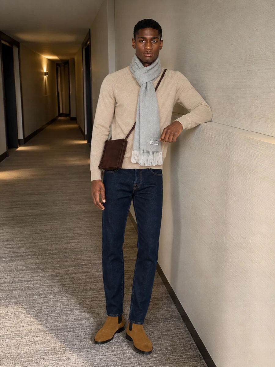 Dark indigo Jacob Cohen denim is paired with a clean beige crewneck for a quietly refined, preppy take on casual days. Camel suede Chelsea boots pick up the warmth of the knit and stitching, while a chocolate suede crossbody and soft grey scarf finish the palette with subtle texture and polish. The result is relaxed enough for weekends yet composed enough for casual Fridays and city dinners.