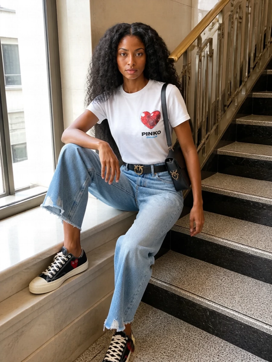 A crisp graphic tee meets cropped wide-leg light denim for a relaxed, sun-ready base that still feels intentional. Black and red canvas sneakers pick up the heart motif, while a structured black shoulder bag and a slim logo belt add just enough polish for city days. The result is sporty, preppy streetwear that reads playful yet pulled together.