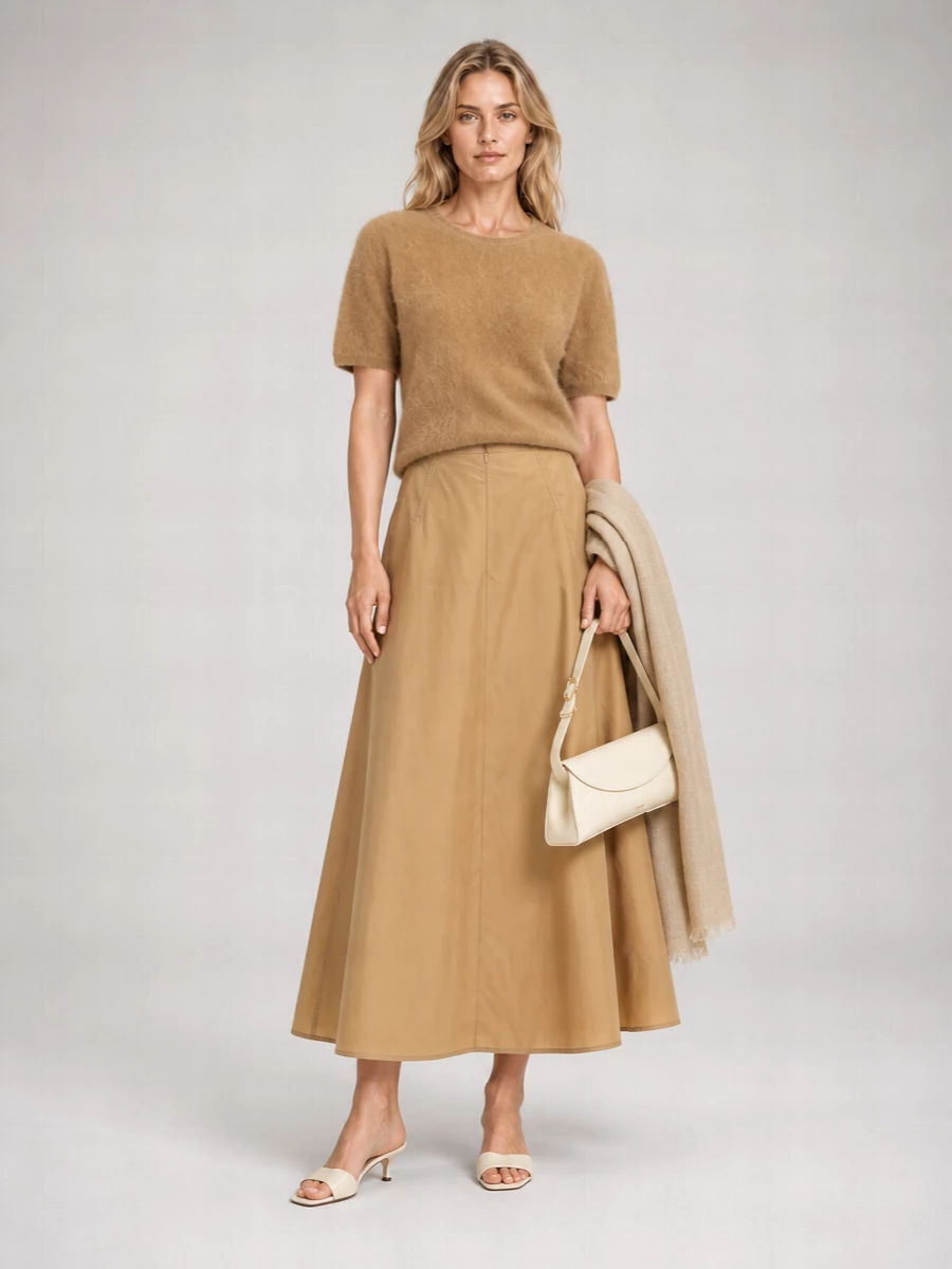 A camel cashmere tee meets a sculpted high-waisted Jil Sander midi for a tonal column that feels calm yet defined. Cream kitten-heel mules and a slim buttercream shoulder bag lighten the palette just enough. The result is a quietly polished neutral ensemble that moves easily from daytime meetings to late lunches with minimal effort needed in styling.
