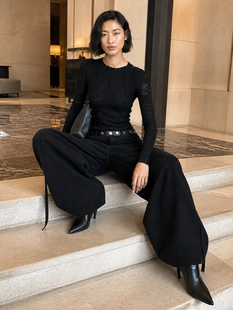 Head-to-toe Attico attitude: inky wide-leg cargos sit low and loose, sharpened by a body-hugging distressed knit on top. Sleek black knee boots elongate everything, while a sculptural black shoulder bag and studded belt keep the mood firmly nocturnal and directional. It is a dark, city-ready mix of volume and precision that feels off-duty but fully intentional.
