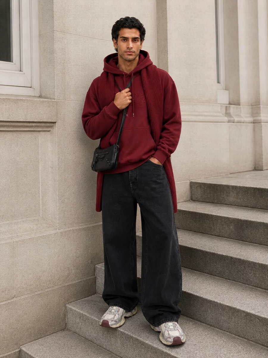 Deep burgundy and washed black set a low-light palette, with the hoodie and wide-leg denim creating that relaxed, directional Balenciaga street frame. Chunky runners in off-white and burgundy echo the top and add sculpted weight at the floor. A slim black crossbody and tonal burgundy scarf finish it with just enough hardware and texture to feel considered but still off-duty.
