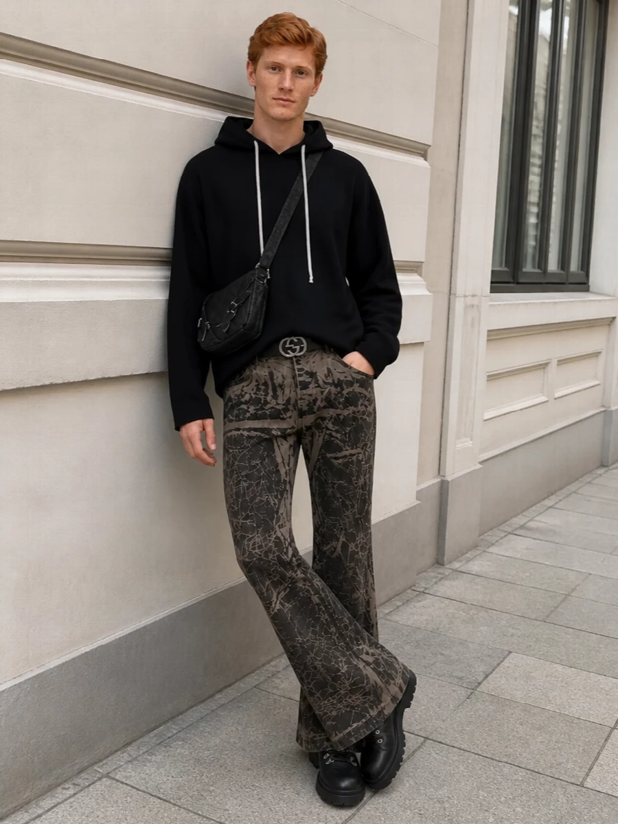 This look pushes the DRKSHDW camo flare into full uniform territory with a relaxed black asymmetric hoodie that keeps the top clean while mirroring the pants’ off-kilter energy. Underneath the dramatic leg, solid black Prada hikers anchor the silhouette with a substantial lug sole, and a compact, dark-toned crossbody plus a discreet logo belt add just enough structure and hardware to feel intentional without diluting the brutal, industrial mood. The result is a cohesive FW street look that feels dark, architectural and distinctly Rick-coded from every angle.