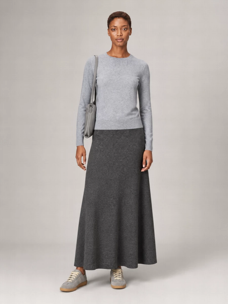 Heather and charcoal greys are stacked in clean, uninterrupted planes so the focus stays on proportion and movement. The high-waisted knit maxi elongates beneath the regular crew, with tonal sneakers and a softly structured shoulder bag keeping the mood calm and considered for city days or travel.