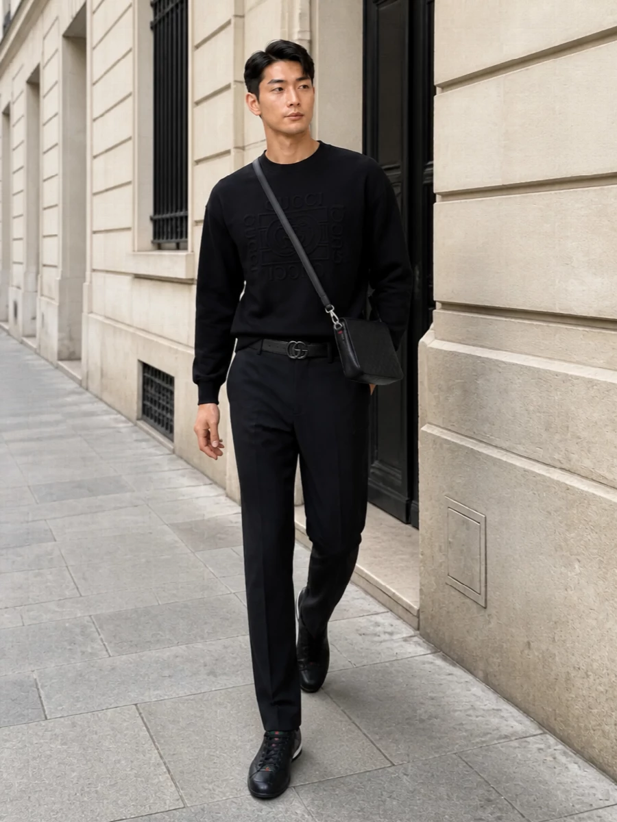 This look builds a sharp monochrome column around the Gucci track trousers, anchored by a tonal black logo sweatshirt for a refined, logo-aware take on off-duty dressing. Sleek black leather low-tops and an embossed crossbody keep everything streamlined and quietly luxurious, while the slim gunmetal-buckle belt adds just enough structure for city-ready polish without breaking the sporty ease.
