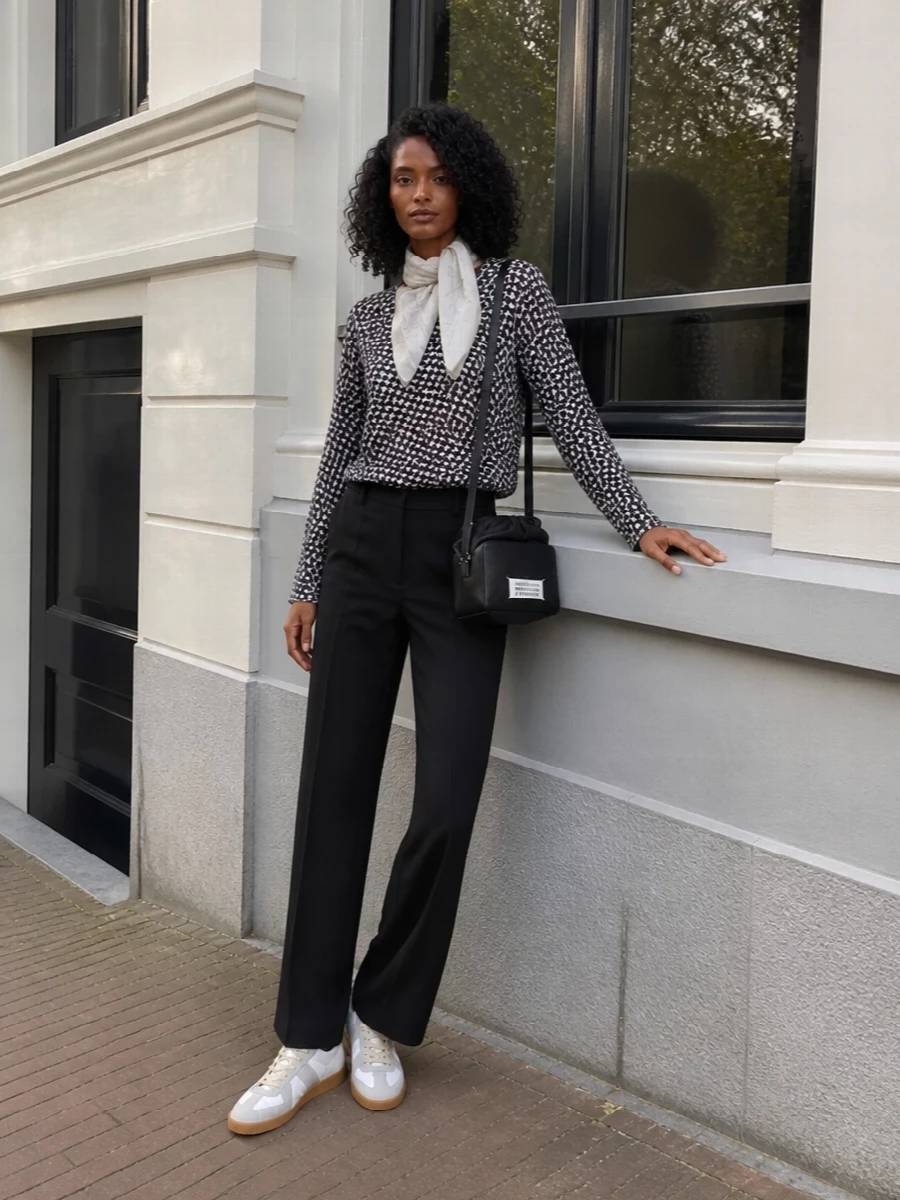 A sheer, graphic Comme des Garçons top sits against relaxed black tailoring for a monochrome silhouette that feels precise but not stiff. Margiela sneakers and a compact crossbody keep the mood street‑leaning and mobile, while the sketch‑print scarf adds a cerebral, art‑school finish. It is an easy uniform for gallery afternoons that can slide into low‑key dinners without changing a piece.