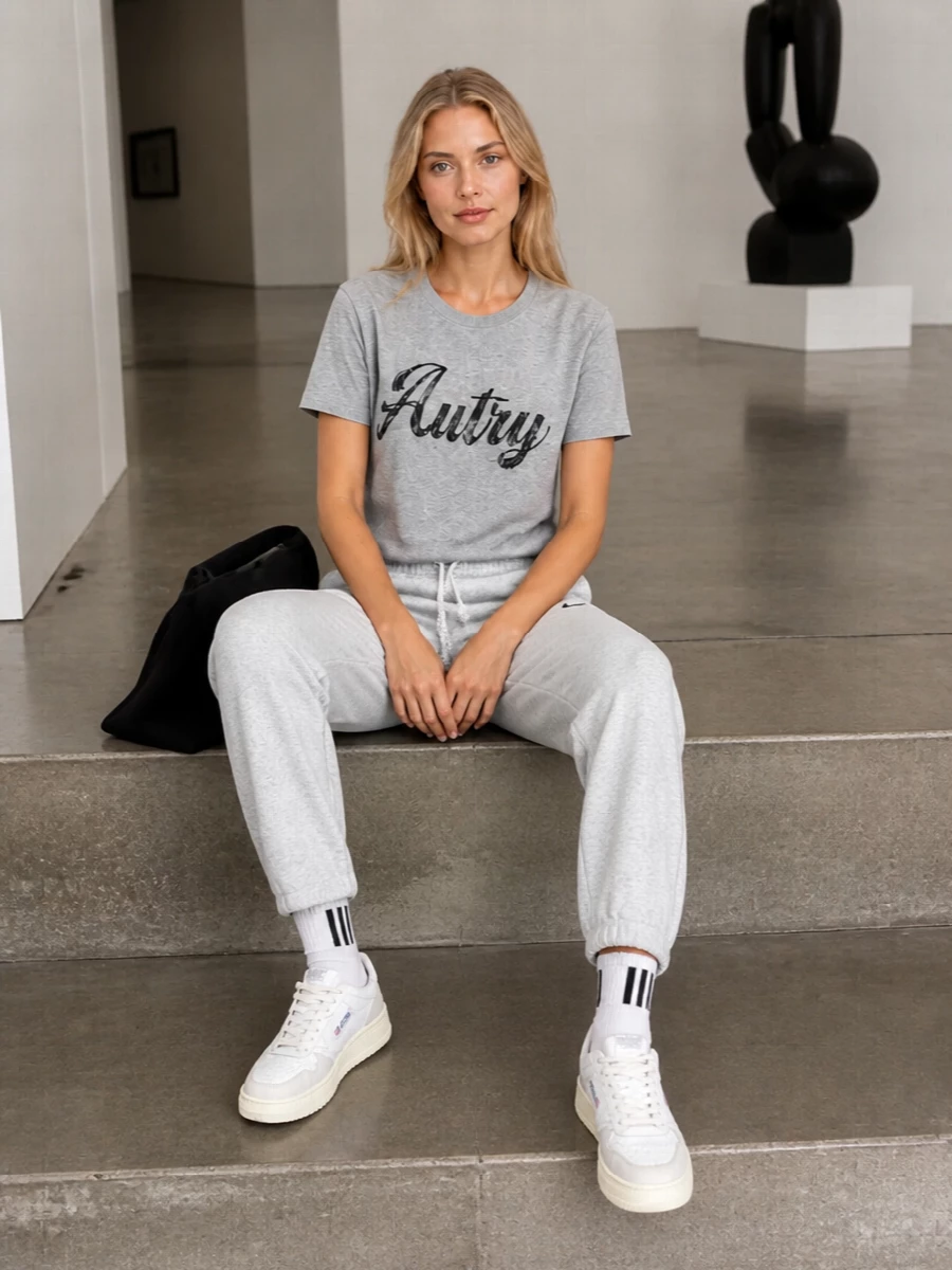 A heather-grey-on-grey base keeps this courtside-inspired edit calm and graphic, with the track pant echoing the tee’s relaxed ease. Neutral Autry sneakers and a compact black shoulder bag sharpen it just enough for city days. Add the striped socks to nod to classic sport styling without breaking the minimalist mood.