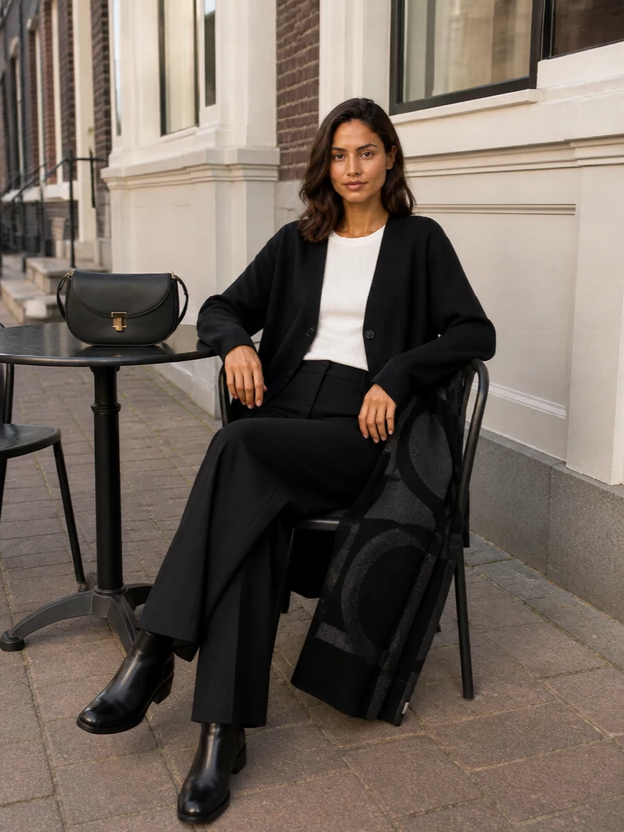 A deep-black Totême column, cut from a clean V-neck cardigan and high-rise wide-leg trouser, reads precise but relaxed for real life. Anchored with polished ankle boots and a sculpted shoulder bag, it moves easily from desk to dinner without breaking the monochrome line. The oversized wrap adds a subtle graphic layer when you want more texture and warmth around the shoulders.