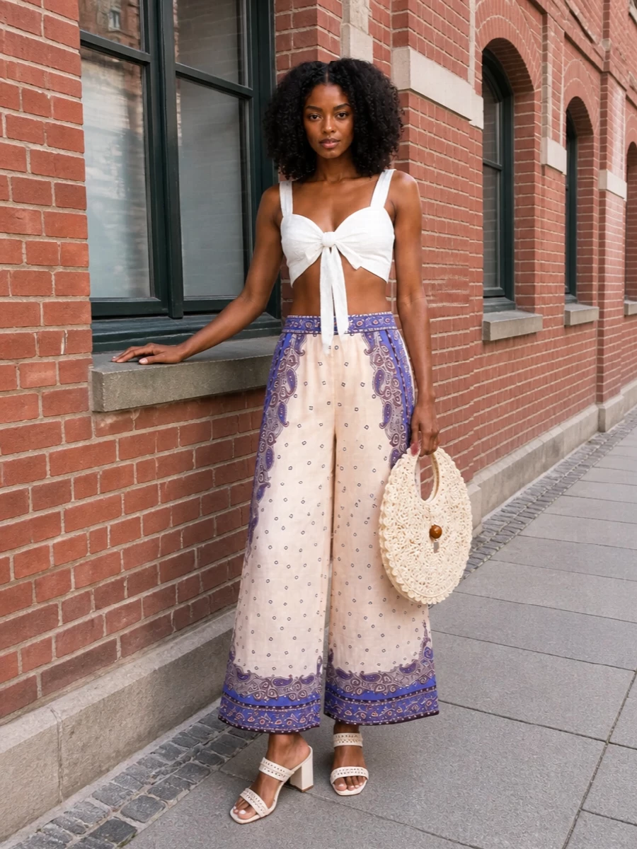 Zimmermann’s paisley cropped wide-leg trouser is paired with a white tie-front bustier to highlight the waist and keep the silhouette fresh, light and romantic. Cream block-heel sandals extend the soft column of color while adding easy height, and a sculptural crochet bag brings in just enough texture for sunlit garden parties or coastal afternoons. The result is a soft, bohemian ensemble that feels dreamy yet quietly polished for warm-weather occasions.