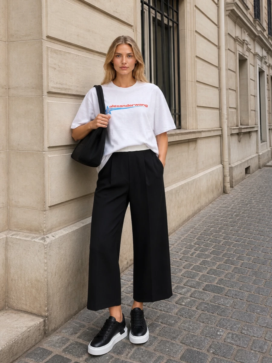 A crisp logo tee and high-waisted cropped wide leg lean into a clean, athletic take on downtown dressing. Chunky black and white sneakers keep the proportions modern, while a soft black shoulder bag and slim monochrome scarf tighten everything into a sharp, city-ready uniform. It feels relaxed and sporty but clearly designer from every angle.