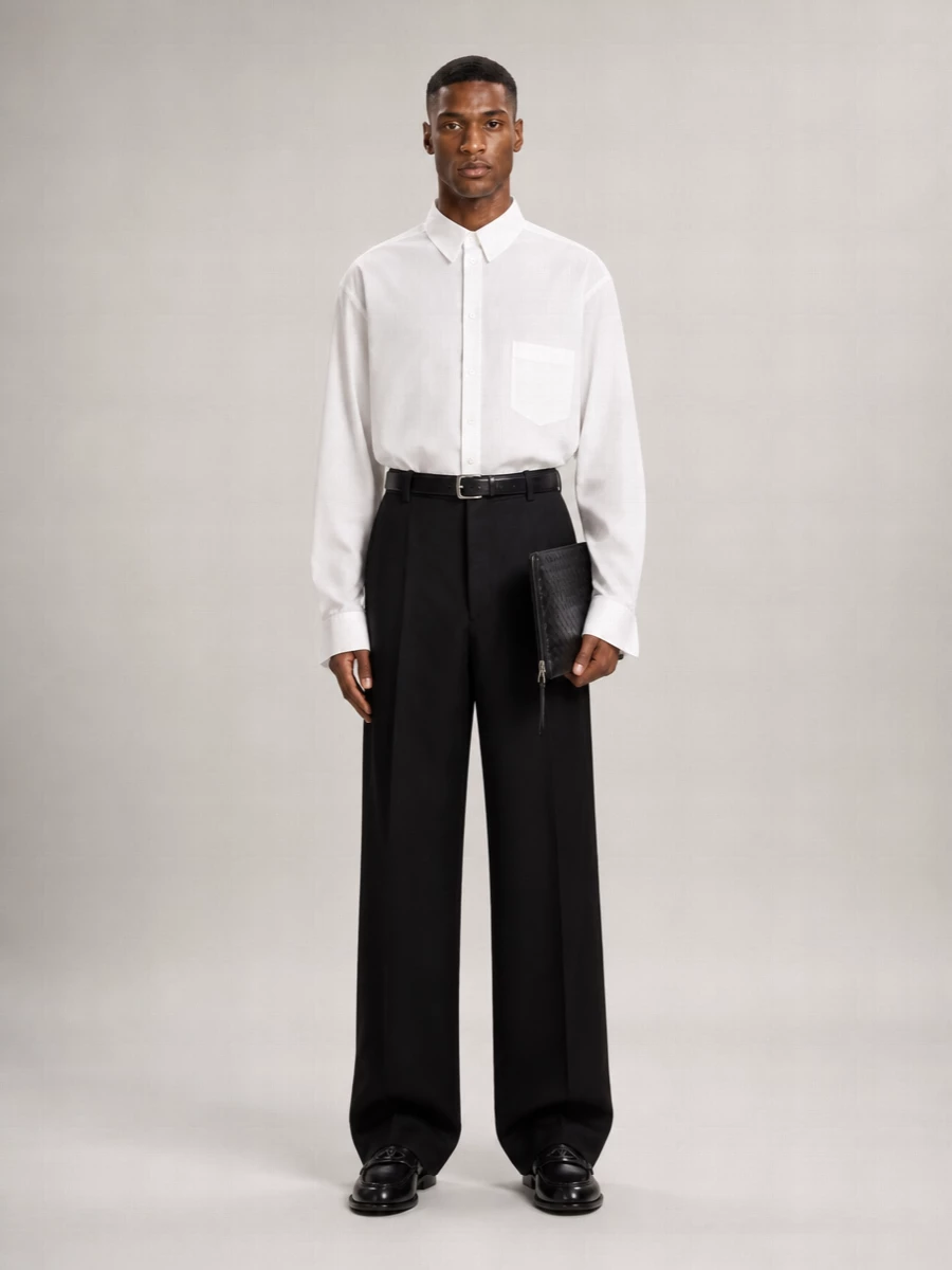Balenciaga’s high-waisted wide-leg trouser is grounded with a crisp, minimally detailed white shirt for a clean, formal base that still carries a quiet attitude. Sleek black loafers and an intrecciato clutch keep everything in a disciplined monochrome story, while a slim black belt sharpens the waist and lets the asymmetric hem read as an intentional design move rather than a quirk. The result is evening dressing that feels controlled, directional and completely logo-light from most angles.