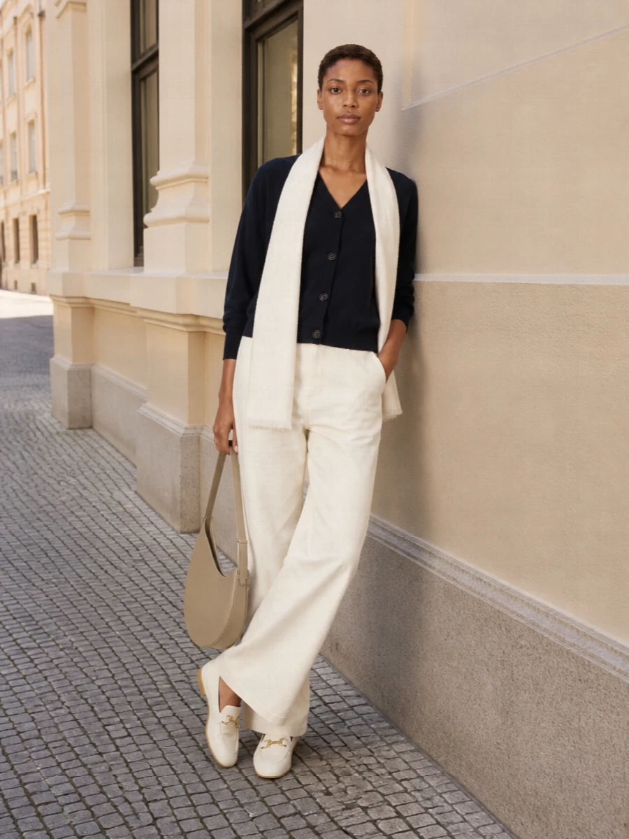 Ink navy and buttercream create a calm, modern palette, with the cardigan relaxed over long, clean trousers for an easy column of color. Cream loafers and a sand hobo keep the mood quiet but intentional, their soft structure echoing the knit’s ease. A gauzy ivory scarf is the final light touch, bringing the neutrals together without adding weight.