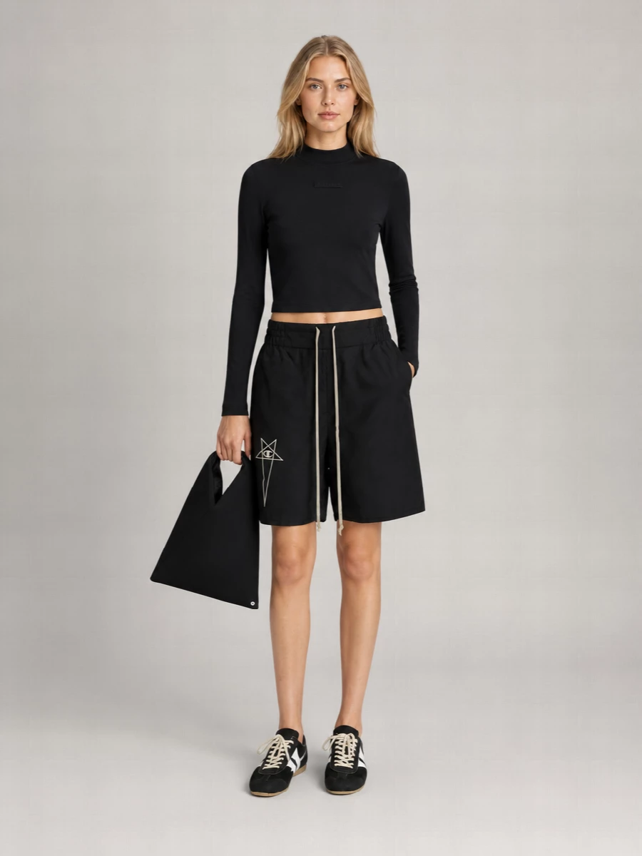 A sharp black-on-black uniform built around the directional knee-length short, grounded by a slim cropped sweatshirt for a clean, athletic line. The low-profile track sneakers and sculptural tote keep everything graphic and intentional, not loud. It reads like off-duty sport with a quiet, designer edge.