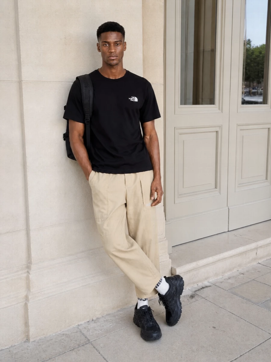 A black North Face tee pairs with light beige technical trousers for a crisp, city-ready spin on outdoor gear. The all-black trail runner and matte technical backpack keep everything grounded and practical. Neutral logo socks tie into the monochrome accents without distracting from the clean, minimal palette.