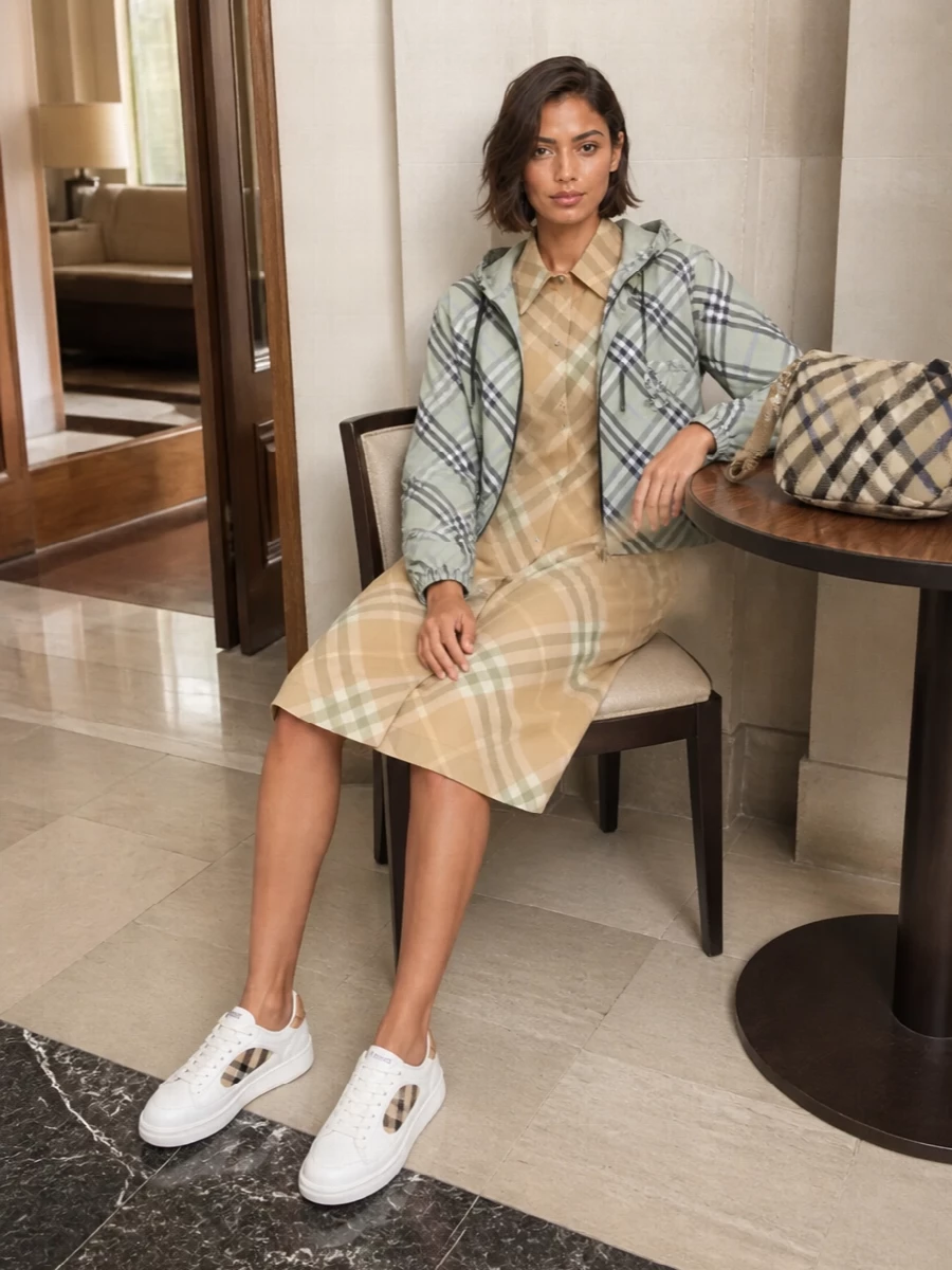 This look leans into a modern Burberry uniform: the pale sage cropped bomber layered over the softly scaled camel‑sage shirt dress for a cohesive play on check and a relaxed, polished SS silhouette. Clean white leather sneakers and a streamlined check cross‑body keep the attitude sporty yet quietly luxurious, letting the layered heritage patterning feel graphic without ever looking overdone.