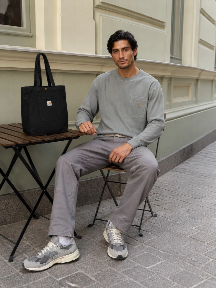 A cool-toned workwear uniform built around muted greys, this pairing keeps the lines straight and unfussy from shoulder to hem. The washed long-sleeve and technical runners sit in the same tonal family as the carpenter-inspired pants, while a black utility tote and sand webbing belt add just enough contrast without disturbing the minimalist streetwear mood. It is an easy all-day combination that reads clean, functional and quietly considered with sneakers and a beanie.