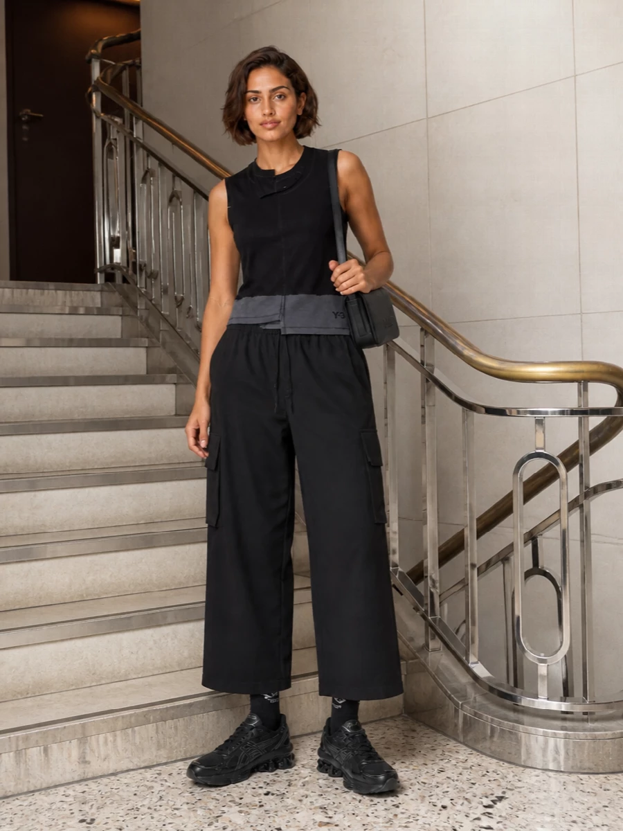 Y-3’s asymmetric tank sits against relaxed black cargos for a graphic top-and-volume base that feels modern, directional and easy to wear. A stealthy black technical runner keeps the energy athletic, while a slim Alexander Wang shoulder bag and logo socks add just enough polish for city days that stretch into late nights.