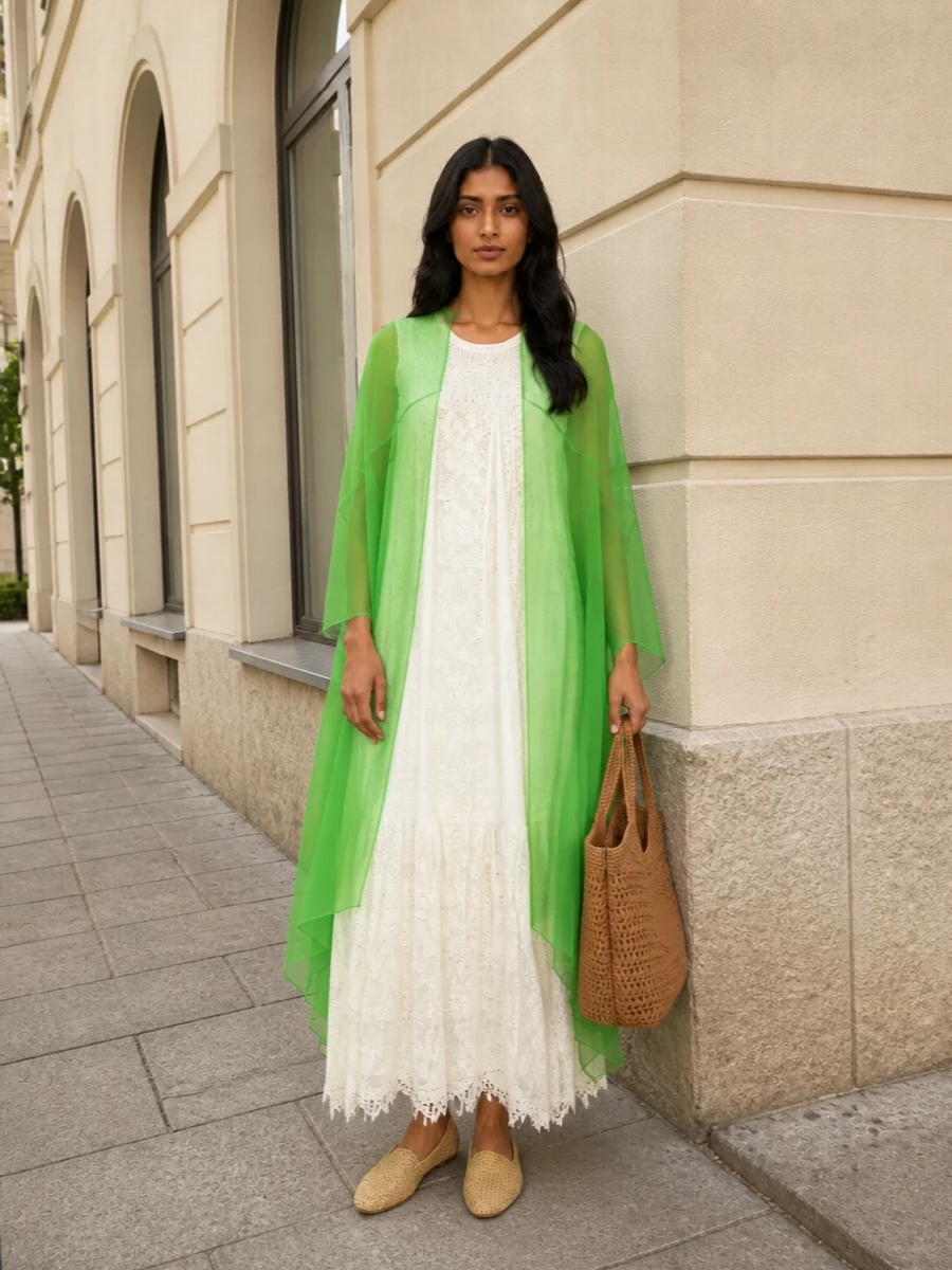 I’m styling the Dries Van Noten poncho over the Paula’s Ibiza ivory tiered dress to lean fully into a romantic, boho resort story rather than breaking the line with a separate top and bottom. The woven Bottega flats and Tod’s tote keep everything grounded in natural, sun-warmed neutrals so the sheer green reads as a single, sculptural veil of color. The result is easy barefoot-garden-supper energy that still feels undeniably high-end and considered.
