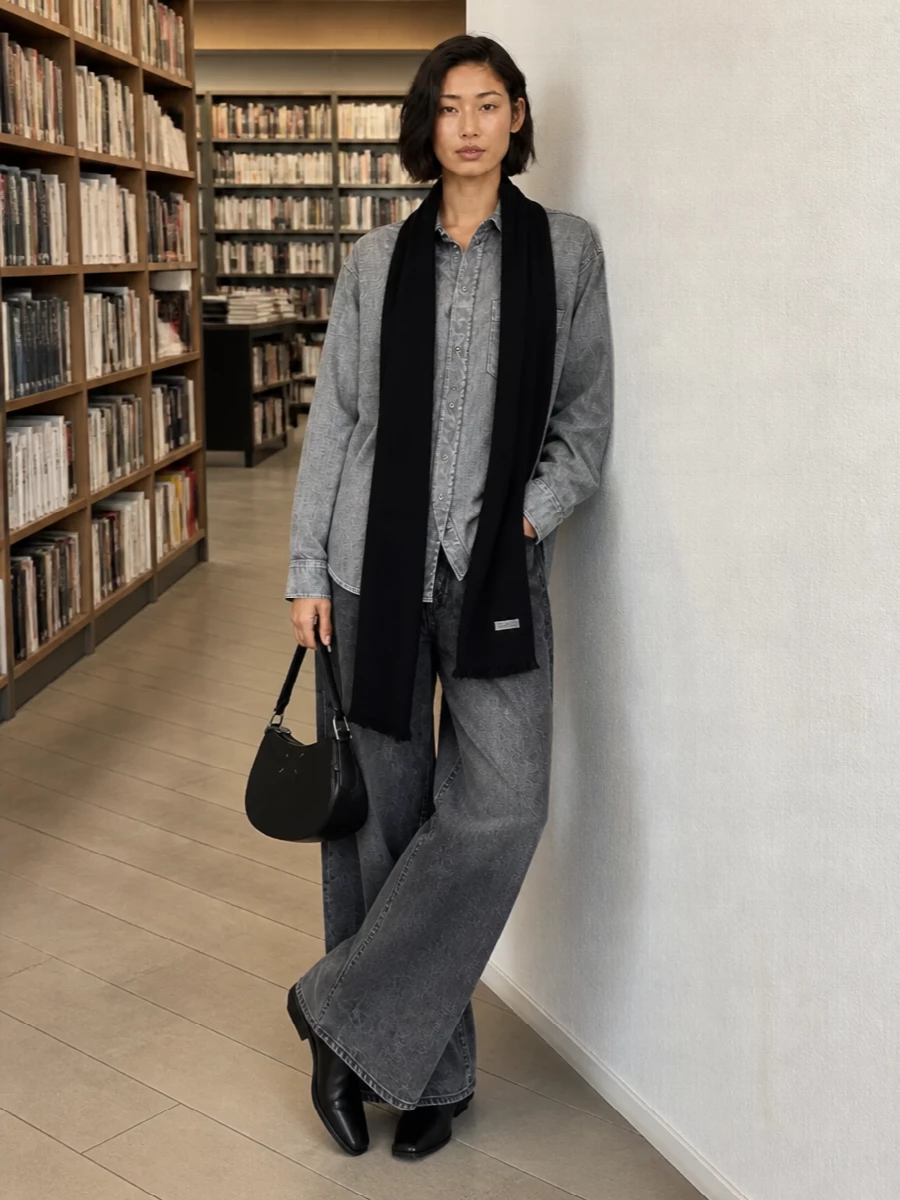 Charcoal wide-leg denim meets a washed grey shirt for a tonal, slightly grunge take on quiet utility, keeping the line long and relaxed. A sculpted black loafer sharpens the proportions, while a compact black crescent bag and ribbed scarf bring in subtle Margiela attitude without disturbing the ease. The result is a city-ready uniform that feels considered yet unforced, ideal for art days, studio visits, or low-key evenings.