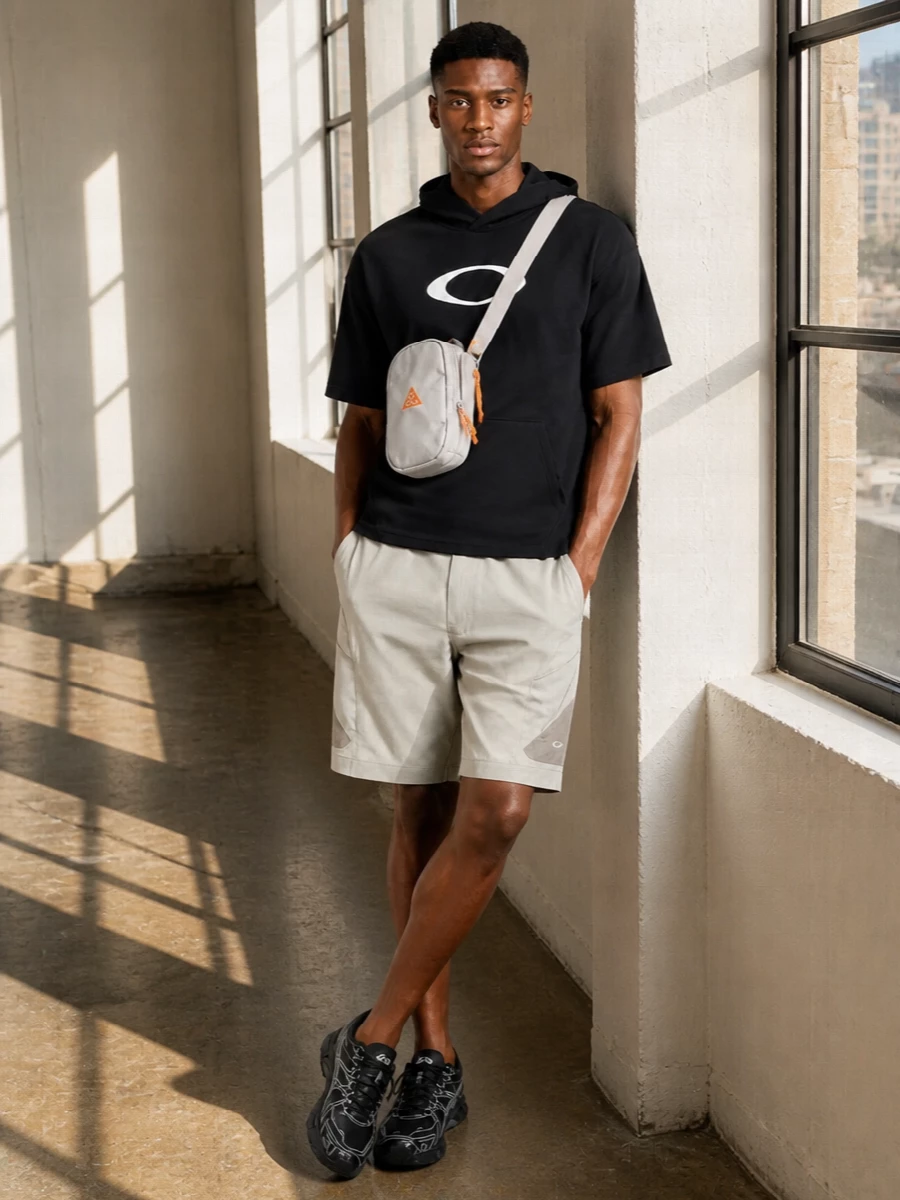 A graphic Oakley hooded tee meets light stone technical cargos for a minimalist street-sport mix that feels ready for city movement and short trail detours alike. Black and charcoal runners keep the energy fast but understated, while the taupe crossbody adds just enough outdoor detail without breaking the clean lines.