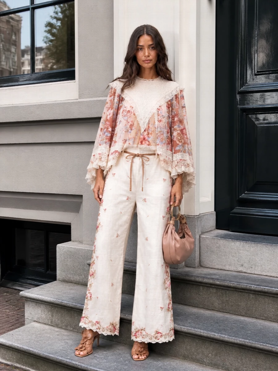 Zimmermann-on-Zimmermann keeps the story cohesive, with the cape-backed blouse floating over high-waisted ivory florals for a soft, elongated summer silhouette. Tan strappy sandals and a blush clutch warm the palette, while a gauzy floral scarf adds an optional, whisper-light layer of romance. It is perfect for garden parties, terrace dinners, or any occasion where you want drama that still feels airy and relaxed.