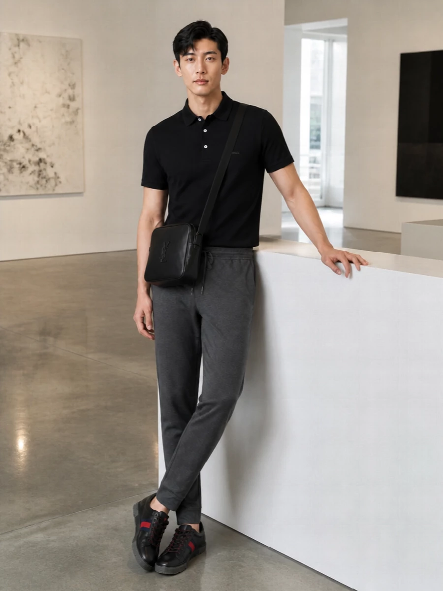 A black Zegna polo and Brunello Cucinelli charcoal track pants bring a sharp, sport-luxe frame to the Gucci sneakers’ red and navy stripe. The Saint Laurent crossbody quietly locks in the monochrome story, so the shoes become the single, decisive hit of color in a clean, modern street ensemble. Slim, tapered lines keep everything feeling intentional rather than relaxed-by-accident.