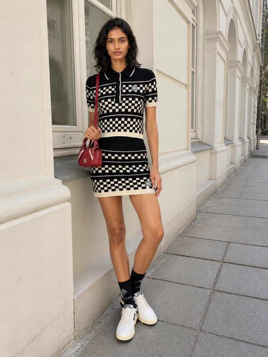 A graphic Amiri mini goes full street-preppy, grounded with monochrome Autry sneakers so the checkerboard feels playful rather than precious. The bandana-wrapped red Amiri bag injects a single bold color hit that still reads cohesive with the logo story. Logo socks peeking above the sneakers keep the whole thing sharp and club-ready without losing its athletic edge.