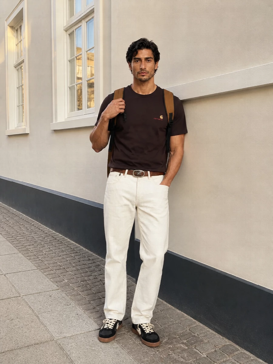 Deep brown jersey sits cleanly against creamy straight-leg workwear trousers for a grounded, everyday Carhartt uniform. Black and cream skate sneakers mirror the top and bottom tones, while a caramel backpack and brown belt reinforce the utility mood without feeling heavy.
