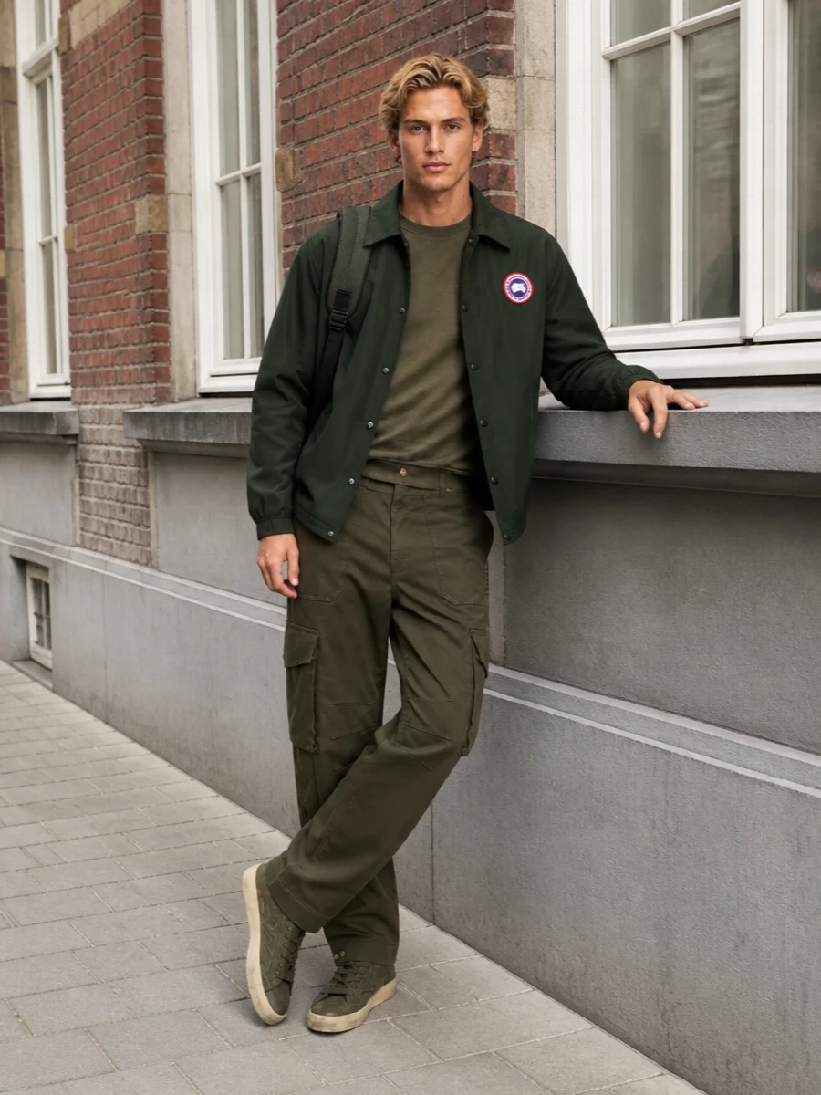 A tightly edited olive story that leans into sport and utility without feeling overdesigned. The mix of Canada Goose outerwear, Golden Goose jersey and cargos, and a Rains technical pack creates a modern city-uniform in one color family, with subtle shifts in texture doing the work. It is relaxed, functional and quietly confident, ideal for off-duty days that still move through the city at pace.