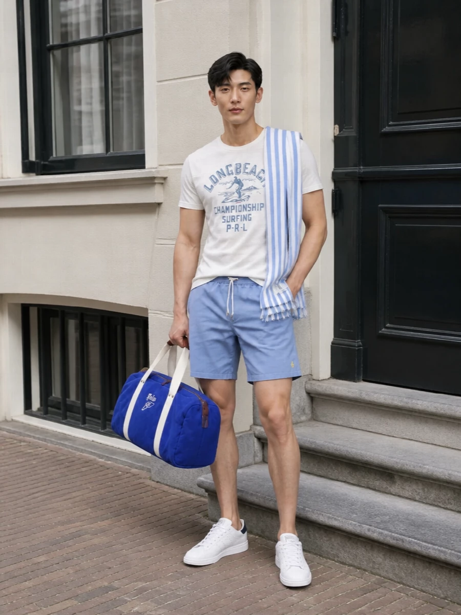 Soft blues and off white keep this Polo surf graphic tee grounded in a clean, coastal palette, paired with powder blue swim shorts for an easy Long Beach mood. Crisp white and navy sneakers add just enough structure, while the royal-blue duffle and striped scarf push it toward a relaxed weekend by the water rather than pure poolside.