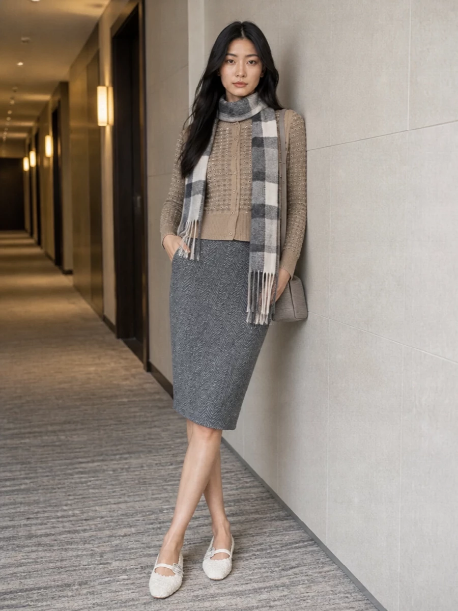 A softly shimmering cardigan meets a tailored grey chevron skirt for a romantic take on office polish. Ivory boucle flats keep the mood gentle and refined, while a compact tweed shoulder bag and tonal check scarf tie the textures together. The result is quietly dressed for city days that can stretch into dinner without changing a thing.