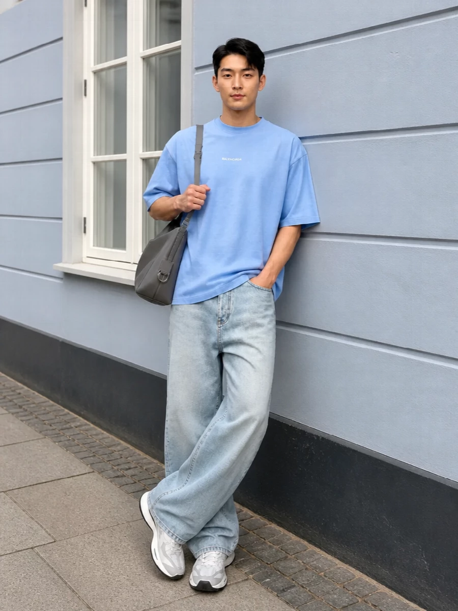 Powder blue and sun-faded denim keep the outfit light and graphic, with the ultra-wide leg echoing the tee’s oversized volume. Clean white runners and soft grey leather ground everything in a technical, modern way, while the structured shoulder bag and retro-sport socks add just enough detail to make it feel intentionally styled rather than casual by accident. It is an easy, high-fashion streetwear uniform that still feels breathable and approachable for warm days in the city.