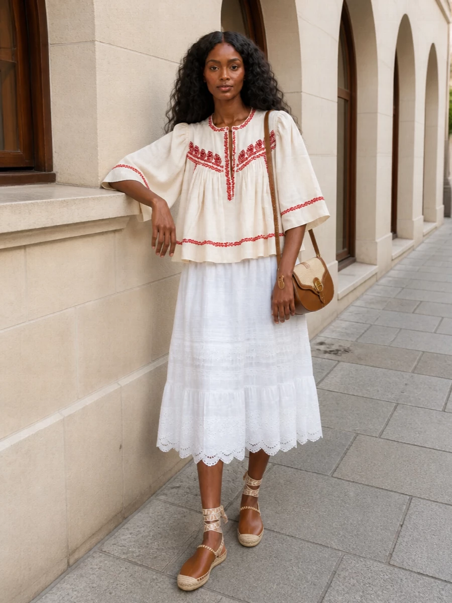 Warm ivory and soft white keep the embroidery and tiers feeling light and romantic rather than fussy. Tan espadrilles and a raffia-detailed saddle bag ground the volume with easy, sun-ready texture while keeping the focus on the blouse’s artisanal detail. It is a softly bohemian summer outfit that works from long lunches to golden-hour walks.