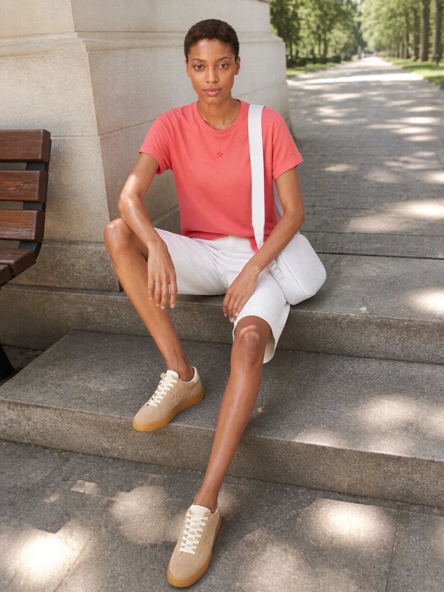 Coral, soft white and sand neutrals keep this tee-and-short pairing fresh and quietly polished for warm days. The tailored knee-length short sharpens the relaxed tee, while neutral suede sneakers and a compact cross-body stay low-key but considered. It is an easy city-ready outfit that feels clean, modern and unfussy.