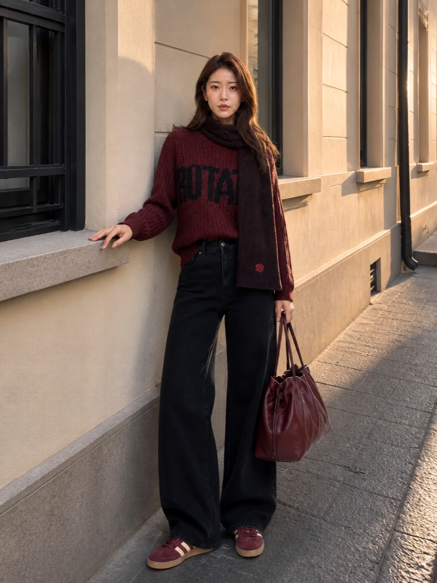 An oversized wine logo knit meets high-rise wide-leg black denim for a laid-back, slightly collegiate streetwear mix that still feels considered. Retro burgundy sneakers keep the color story coherent and casual, while the slouchy burgundy tote and melange scarf lean it into rich, city-ready winter days. The proportions stay relaxed and long-lined, so the outfit feels easy to move in but visually sharp from head to toe.