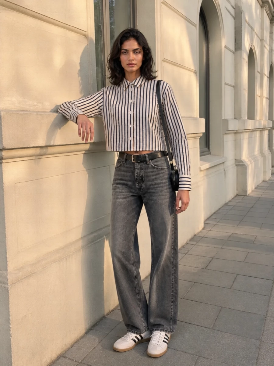 Washed charcoal denim and the cropped striped shirt create a clean, slightly boxy line that feels easy but considered. Neutral retro sneakers keep the energy relaxed, while a small black crossbody and slim belt add just enough structure for all-day city wear.