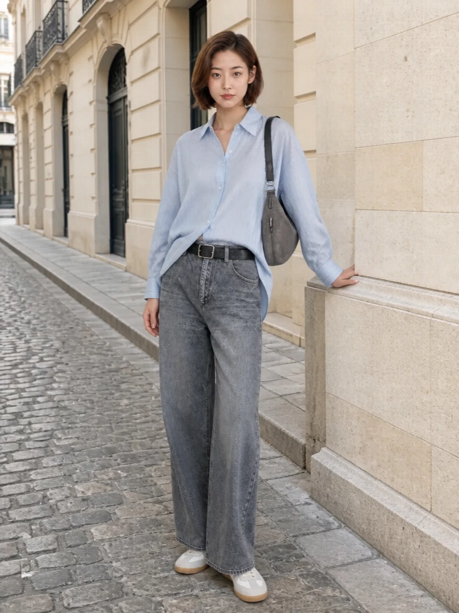 Charcoal wide-leg denim anchors an oversized striped shirt in a slouchy, almost borrowed-from-the-studio proportion, dialed in at the waist with a clean black belt. Off-white Margiela sneakers keep the palette soft and modern, while the Lemaire crescent bag echoes the washed greys for a quiet, artful take on luxury streetwear. The result is relaxed and polished at once, ideal for city days when you want ease with intention.