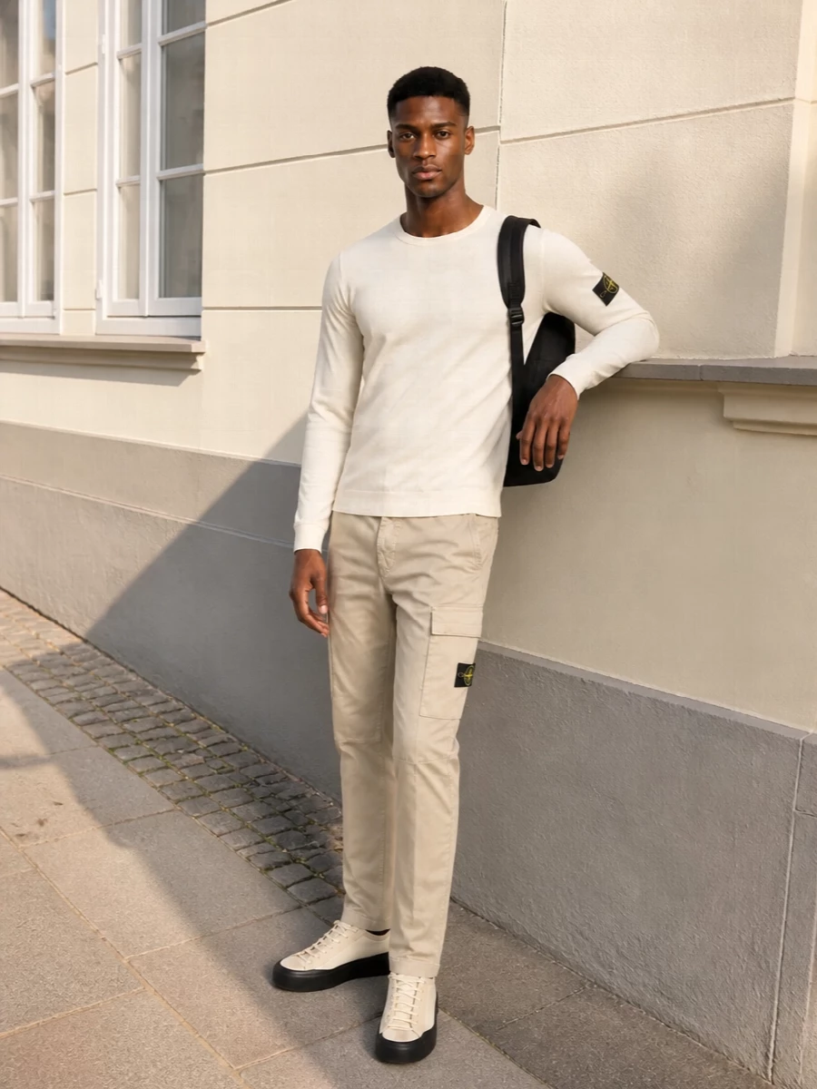 Cream Stone Island jersey with stone cargo trousers and neutral tech runners sets up a calm, tonal street uniform. The black backpack and compass badges echo each other, giving a tight graphic rhythm without crowding the outfit.