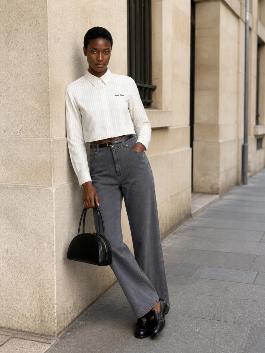 Slate-grey wide-leg denim is sharpened with a cropped, pinstriped shirt that neatly cuts the volume at the waist, creating a long, clean line. Black loafers, a sculptural black crescent bag and a slim leather belt keep the palette restrained and the mood intelligently polished, for a refined SS city uniform that feels effortless yet deliberately put together.