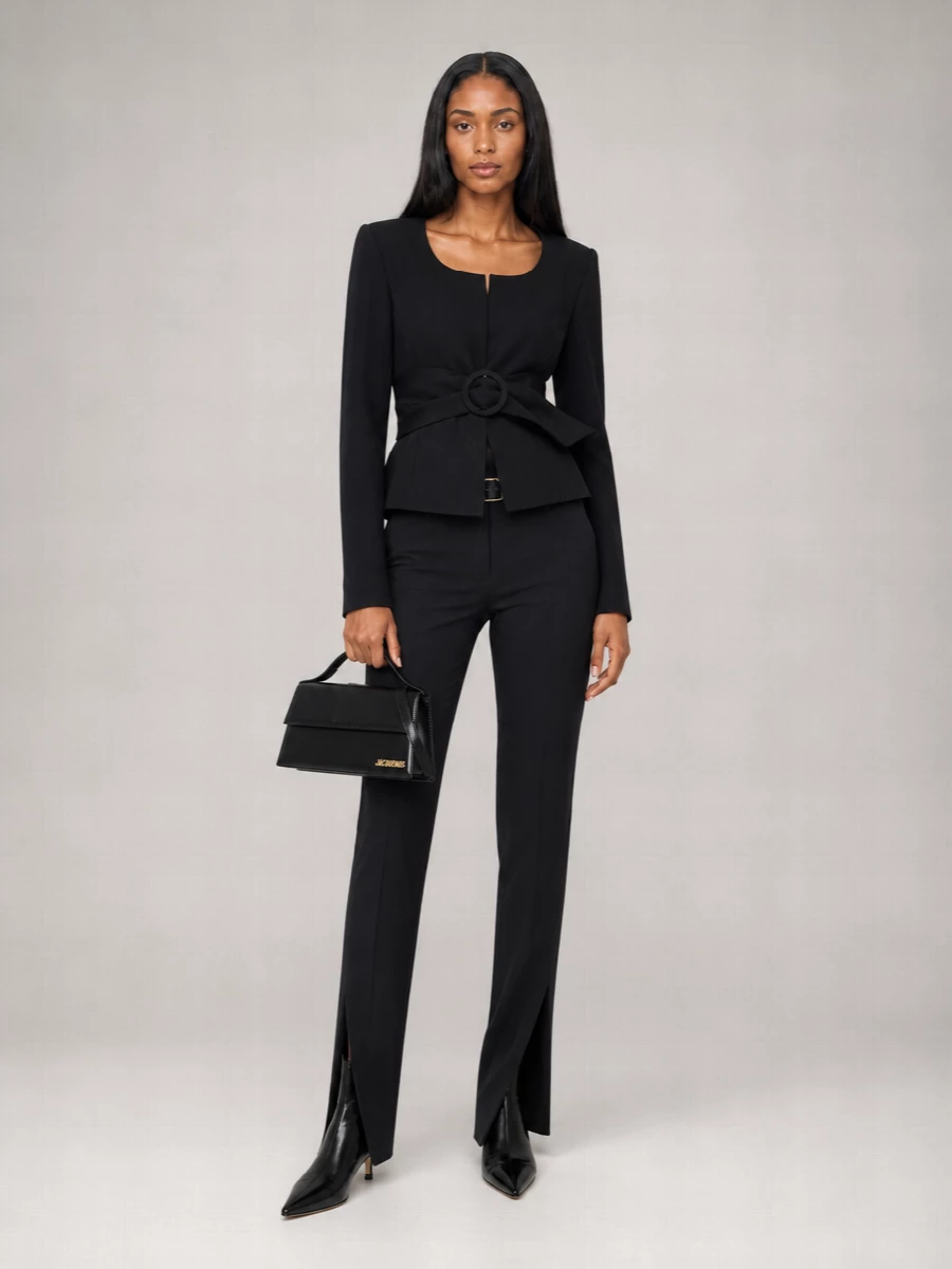 High-waisted slit tailoring meets a sculpted, belted jacket for a black-on-black column that feels sharp, feminine and quietly sensual. A sock-fit kitten heel and small structured top-handle keep the lines long and clean, while the wide belt adds a precise, almost corseted focus at the waist. It is the kind of evening-ready uniform that moves easily from a serious dinner to a late gallery opening without ever looking overdone.
