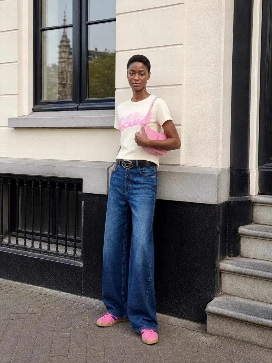 Soft butter cream and bubblegum pink sit on top of wide-leg mid-blue denim for a nostalgic Diesel take on casual Y2K. A vivid pink sneaker and matching glossy baguette amplify the color pop while the logo belt tightens the waist so the relaxed shapes still feel intentional. It is easy, graphic and ready for off-duty city days that still read fun and styled.