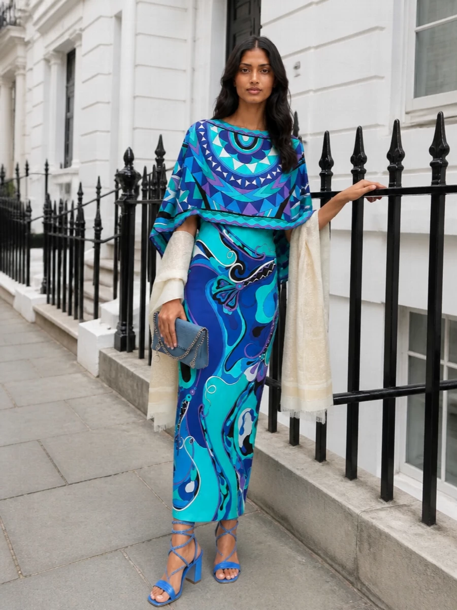 A high-summer Pucci column takes center stage, its oceanic blues echoed by electric Rene Caovilla spirals and a cool Stella McCartney clutch. The result is evening-glamorous yet fluid, with every accessory chosen to support the print rather than compete with it. A whisper-light neutral stole softens the shine, giving you just enough coverage without losing the dress’s movement and drama.