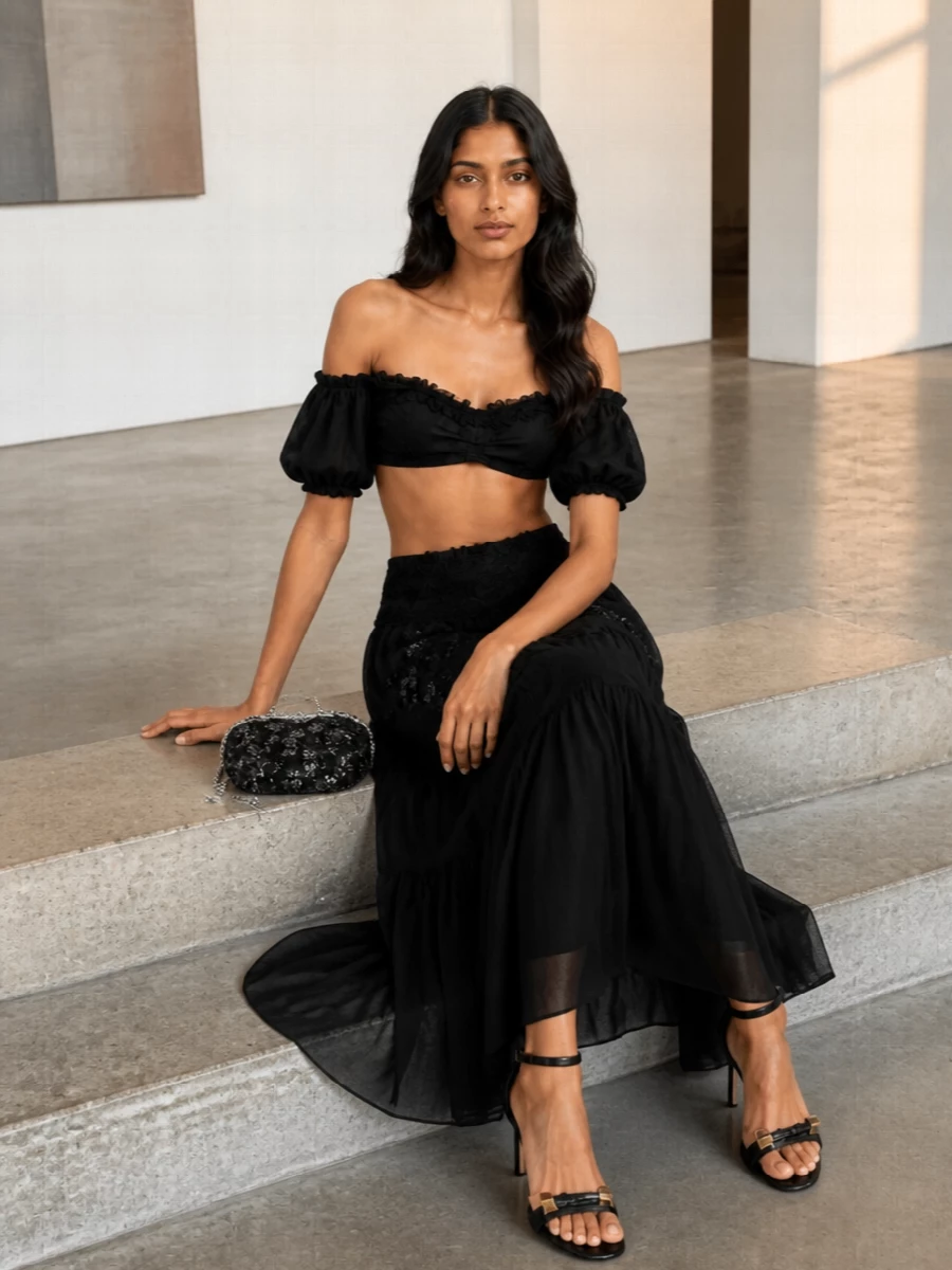 A sultry Ermanno Scervino summer set, pairing the cropped off-shoulder top with a sheer tiered maxi skirt, leans into dark romance with plenty of movement. Fine black stilettos and a jeweled box clutch keep the silhouette long and clean while introducing just enough shine. The rose-print scarf is your styling wildcard, wrapping into hair or hardware to echo the romantic mood in a softer, directional way.