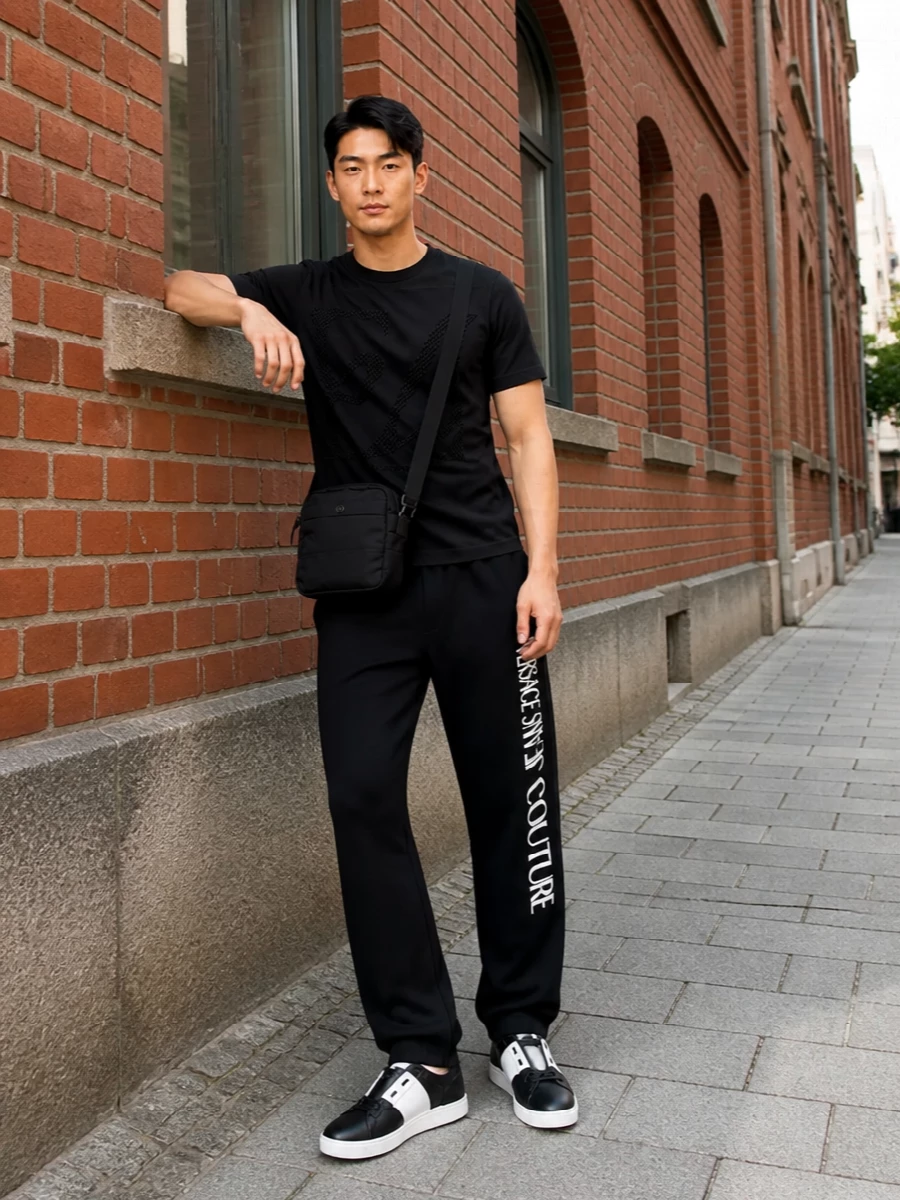 Emporio Armani’s graphic tee stays front and center against clean black Versace track-style trousers, keeping the energy sharp and street without going loud. Valentino’s monochrome sneakers refine the base with a crisp, low-profile line, while a compact Stone Island crossbody adds just enough utility to feel city ready. The result is a modern all-black streetwear set that reads considered but easy for day-to-night wear.