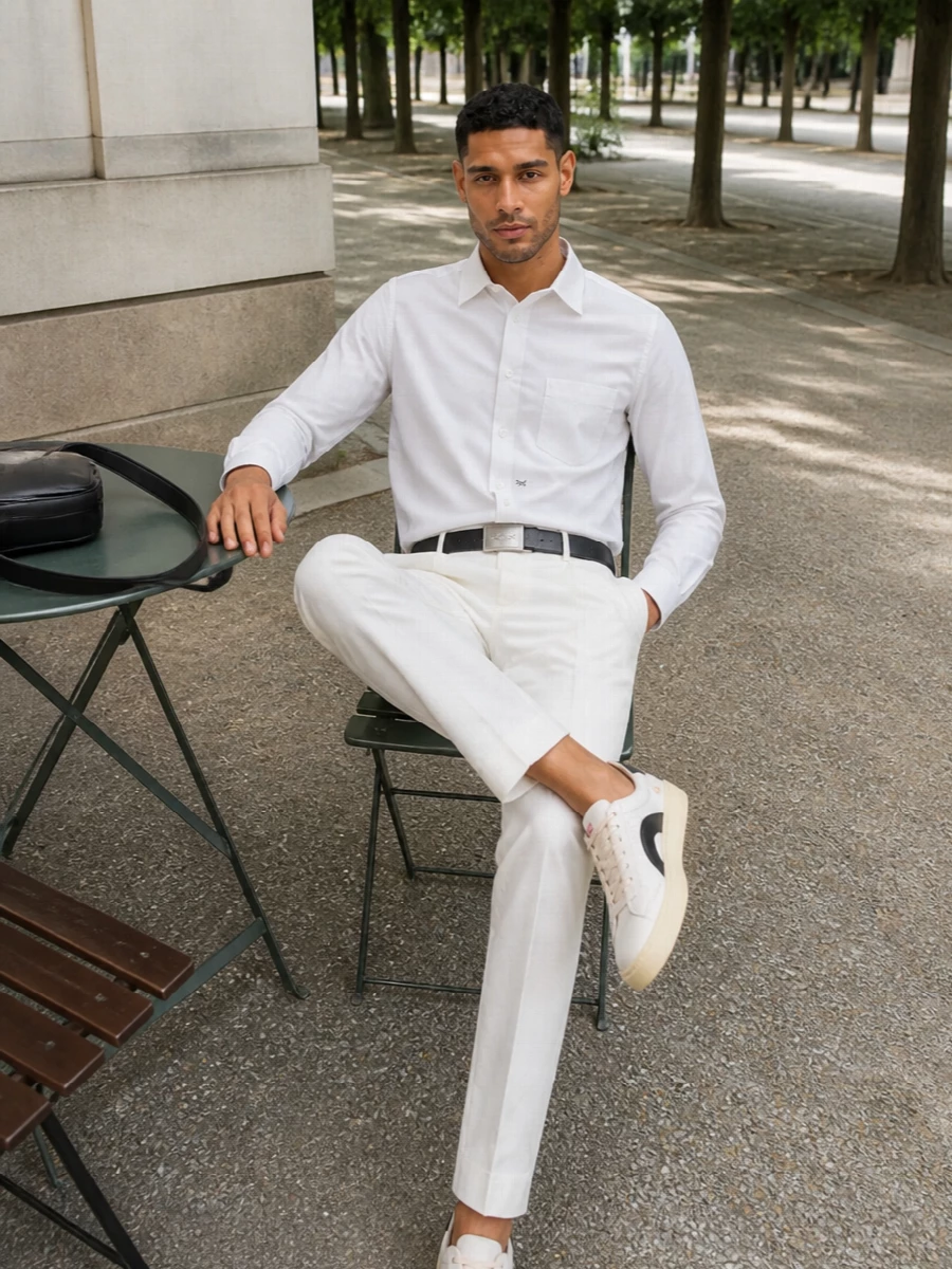 Crisp and graphic, this outfit leans into soft whites with a cropped shirt and pleated trouser that read tailored but still relaxed. Cream and black court sneakers keep it modern and easy, while a slim black belt and compact leather crossbody add quiet structure and city polish. It is a sharp warm weather uniform for days when you want street energy with a precise, preppy finish.